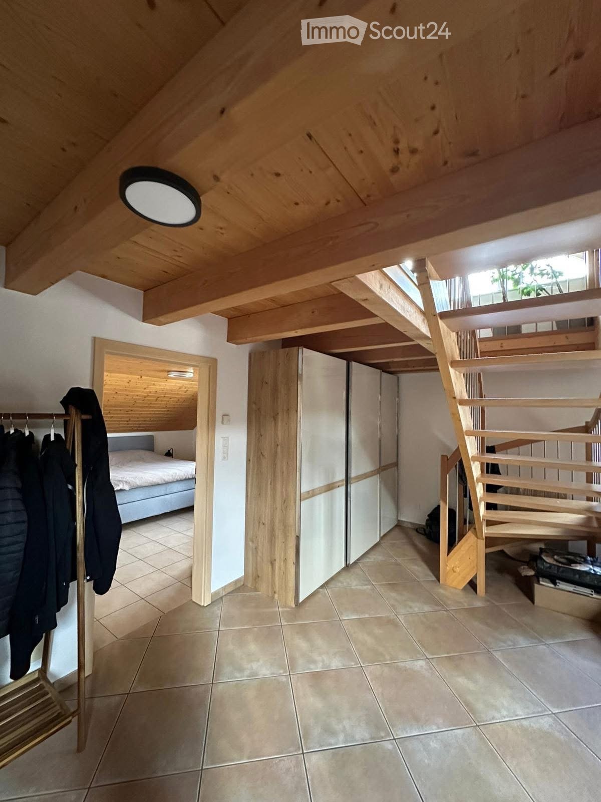 bedroom with a bed, wardrobe, wooden stairs, clothes rack, and ceiling lamp