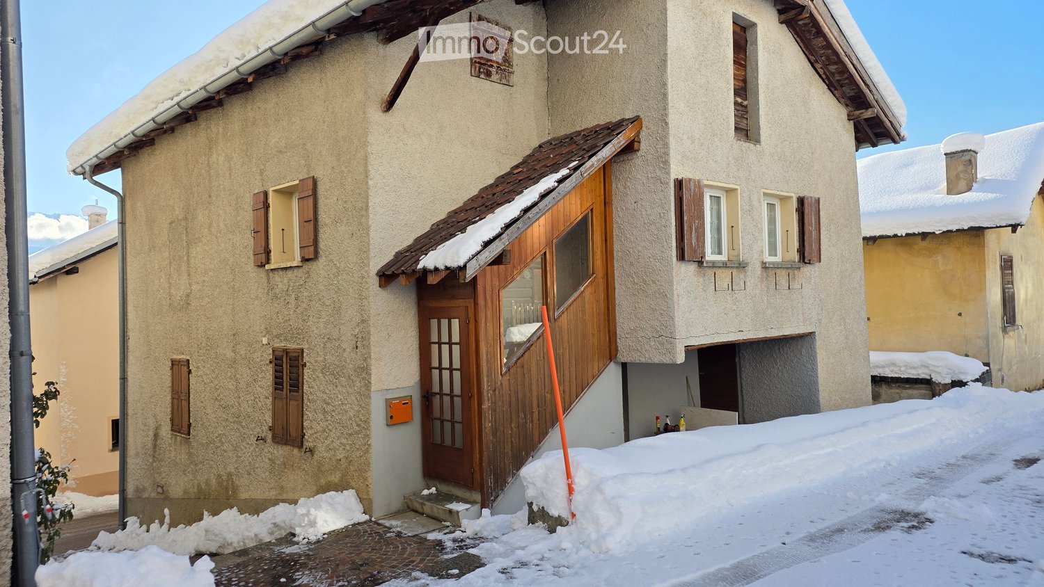 Two story house with wooden front door, brick wall, wooden window shutters, snow covered roof and yard