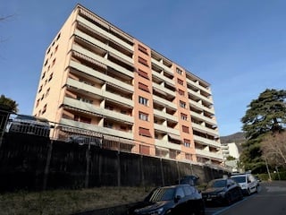 High-rise apartment building, with multiple balconies, several floors, parked cars in front.