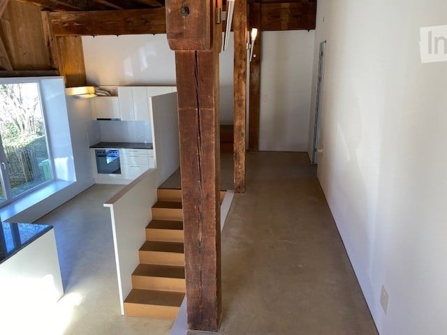 empty room with wooden beams, white walls, tiled floor, stairs, kitchen with oven
