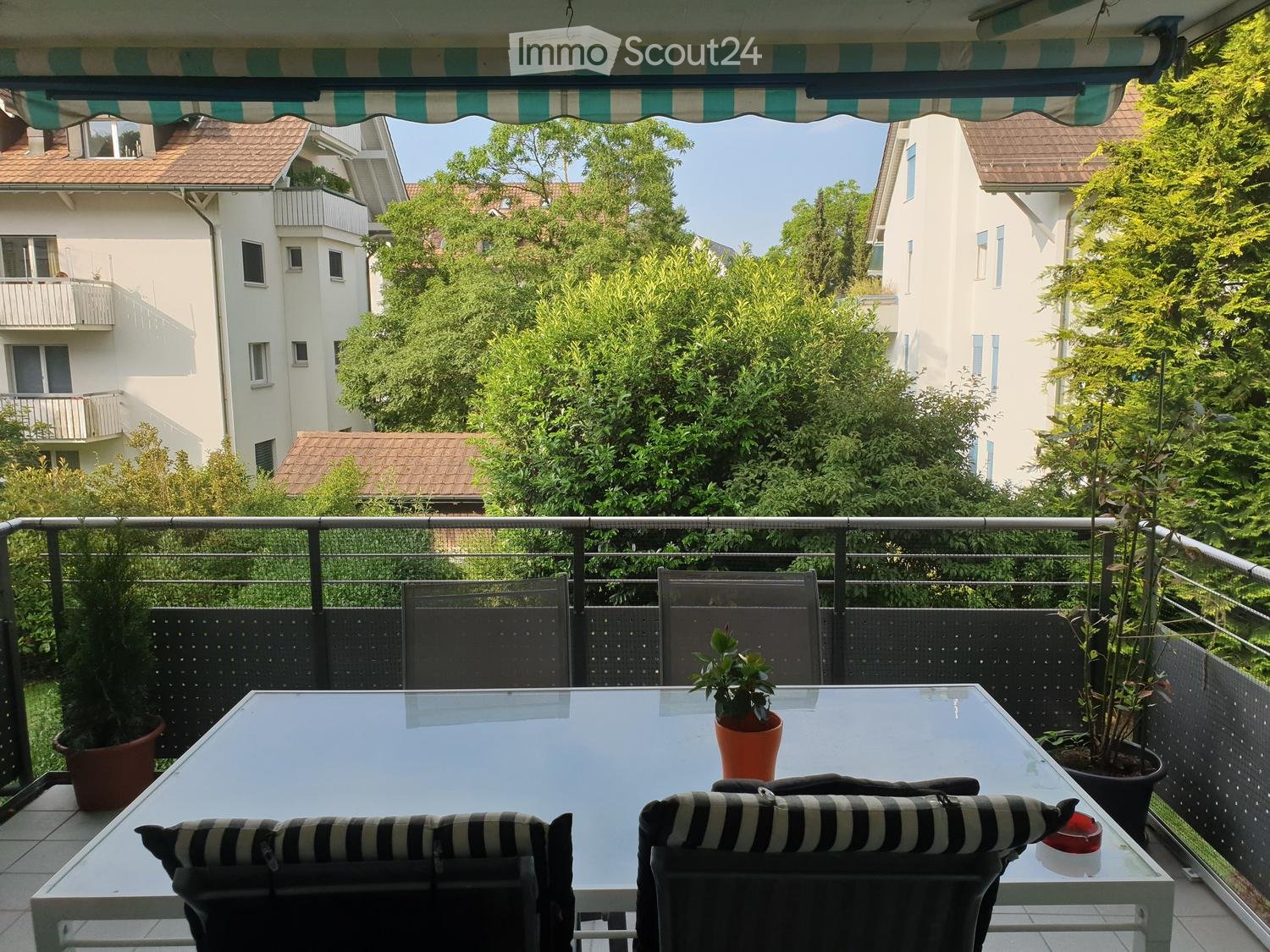 Outdoor table with 4 chairs, balcony, black and white cushions, plants, trees, view of buildings