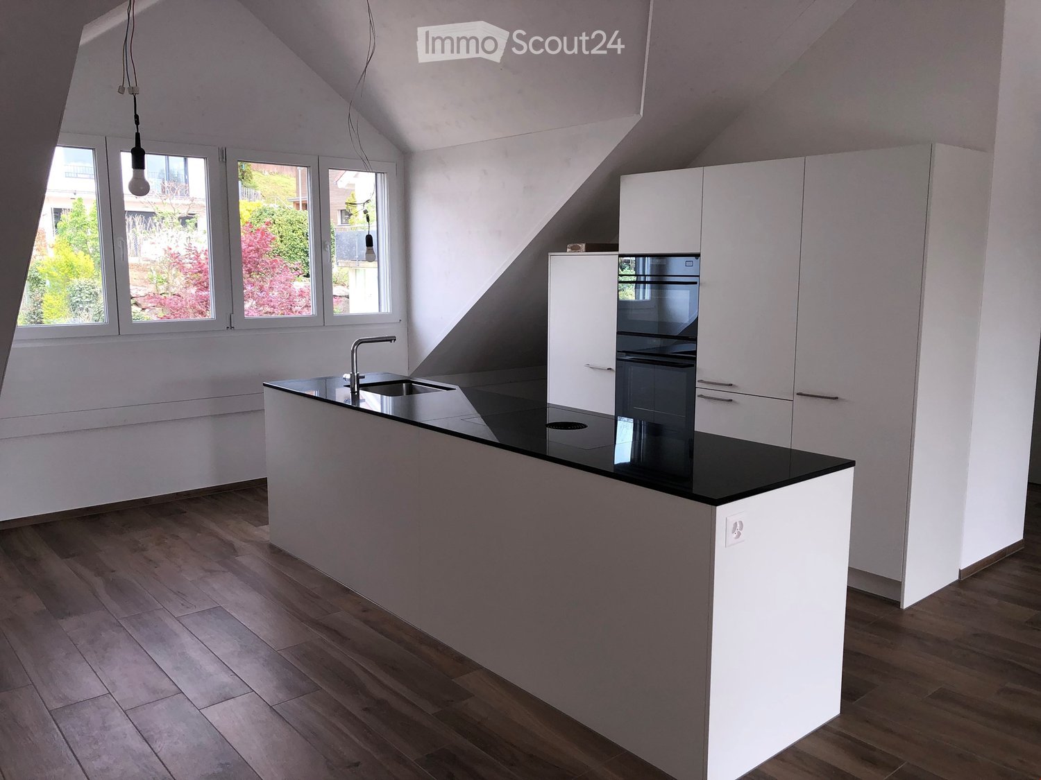 modern kitchen with island, black countertops, stainless steel sink, wooden floors, white cabinets, large windows