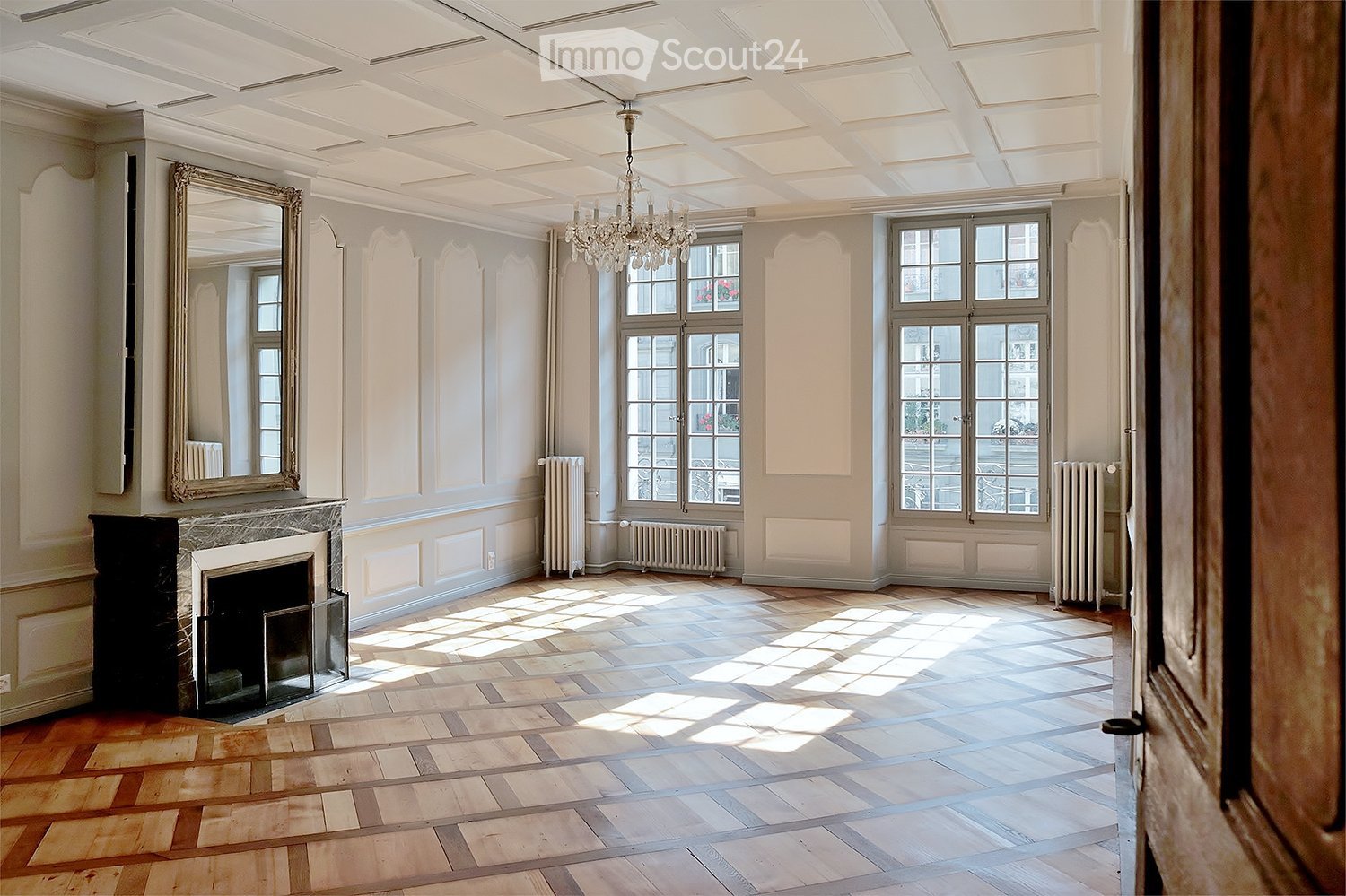 Large room with wooden parquet floor, fireplace, white walls, large windows with doors to the outside