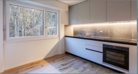 A modern kitchen with wooden floors, white cabinets, a large window, an oven, a sink, and a faucet.