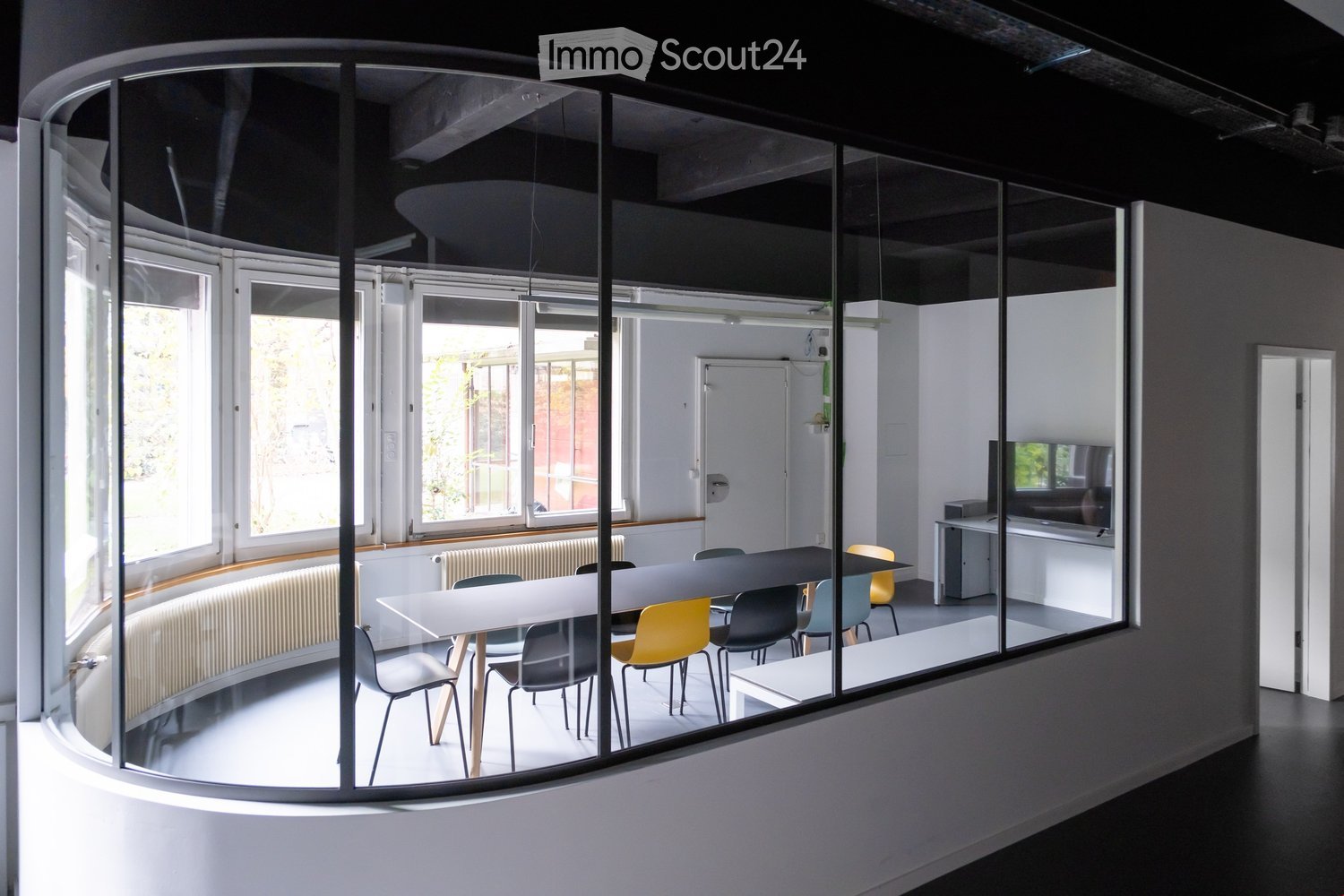 Curved glass wall, round layout, long table with chairs, white walls, large windows, radiators, white floor, furniture