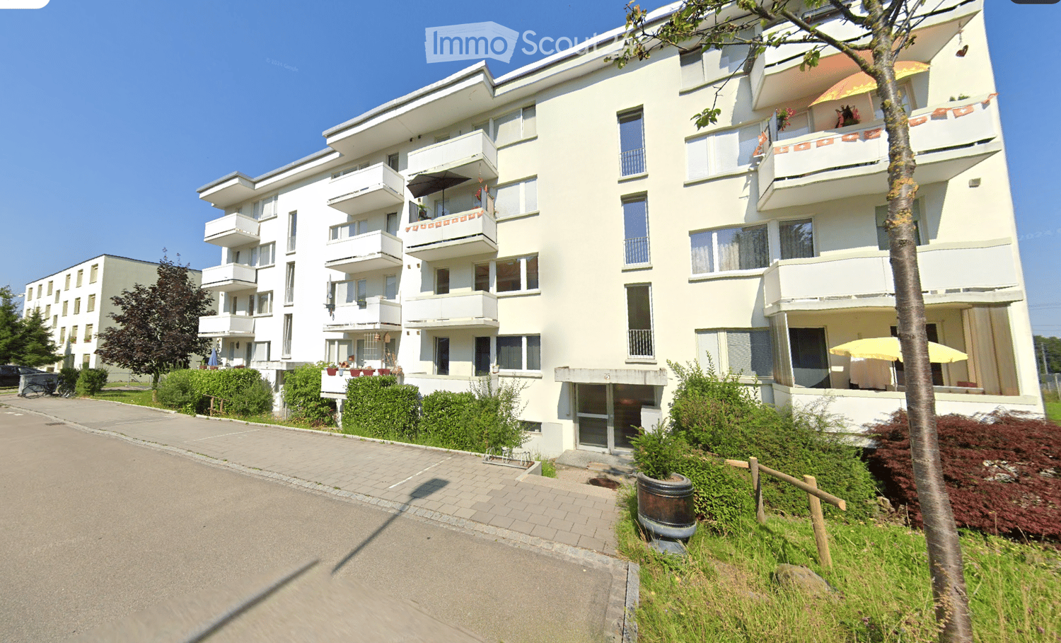 white building, balconies, multiple floors, paved walkway, trees, grass, bushes