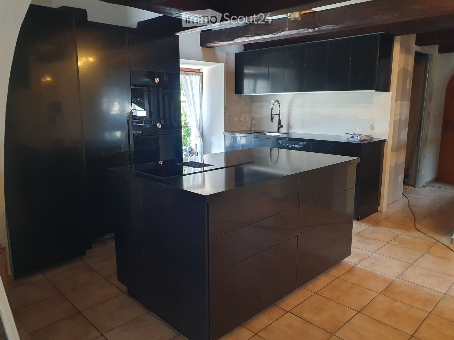 black kitchen island, modern built-in appliances, open shelving, wooden beams, tiled floor