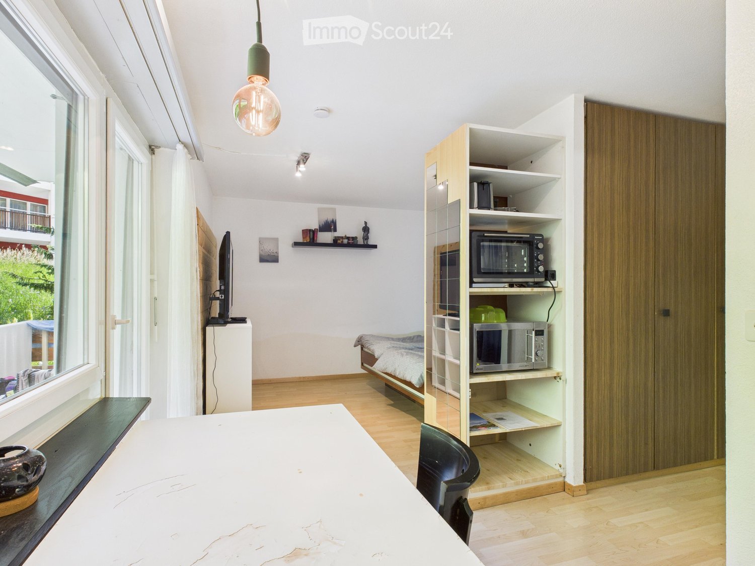 a room with bed, microwave, a TV, a window, a table, a shelf and lamp