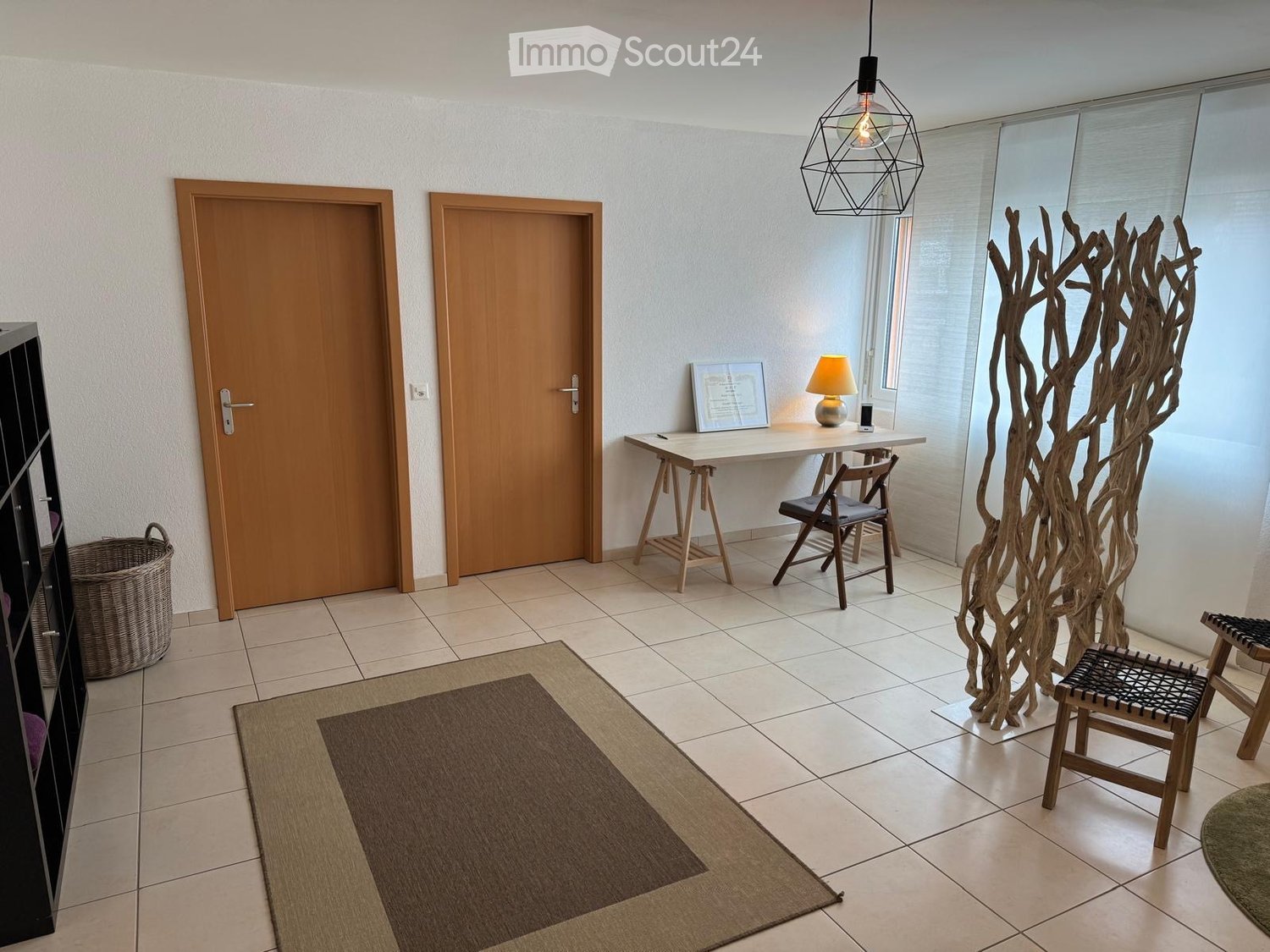 Entrance room with two doors, rug, wooden desk, chair, lamp, shelves, basket