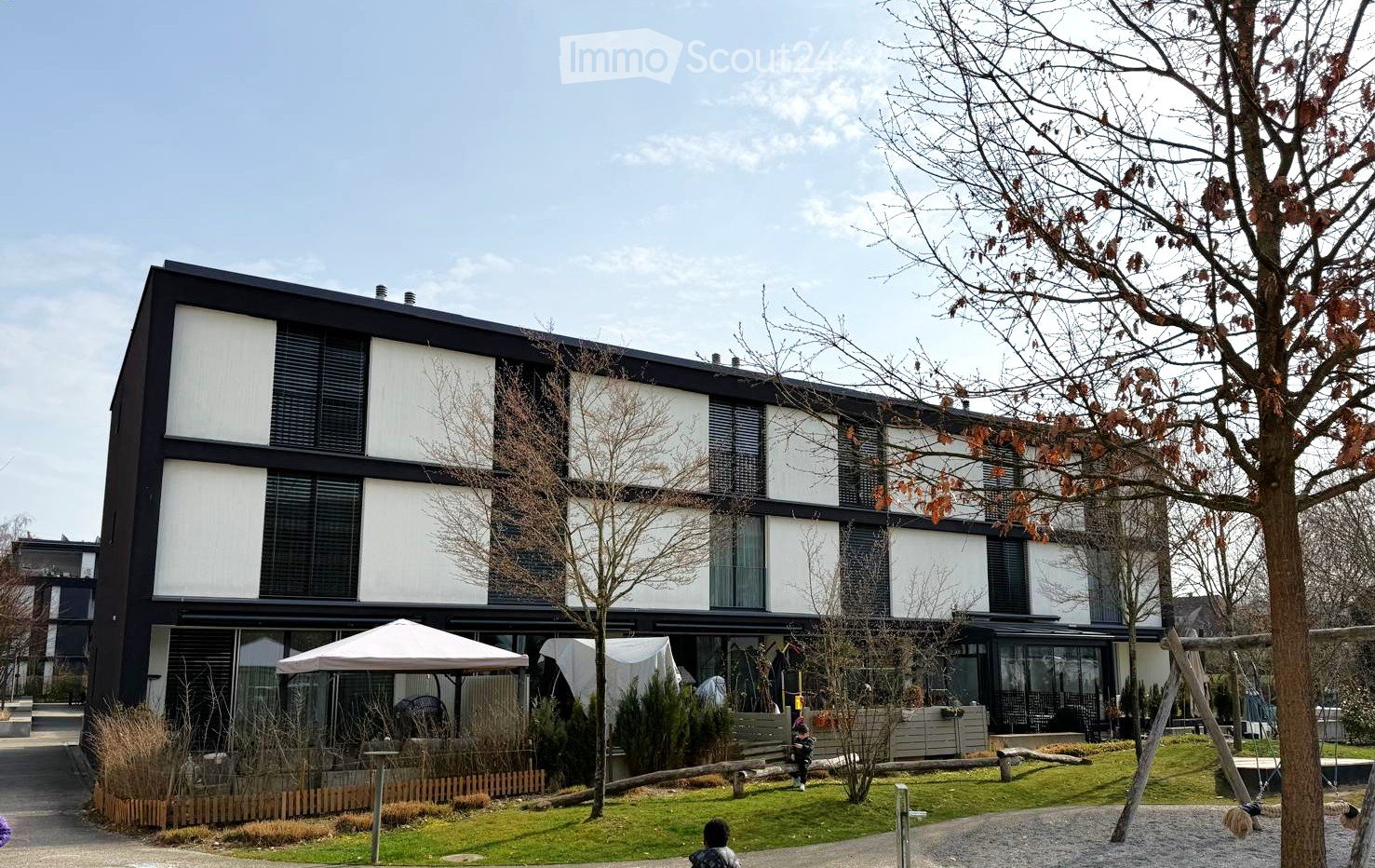 modern building, white and black, glass windows, several floors, surrounding garden with trees and plants, some outdoor seating area