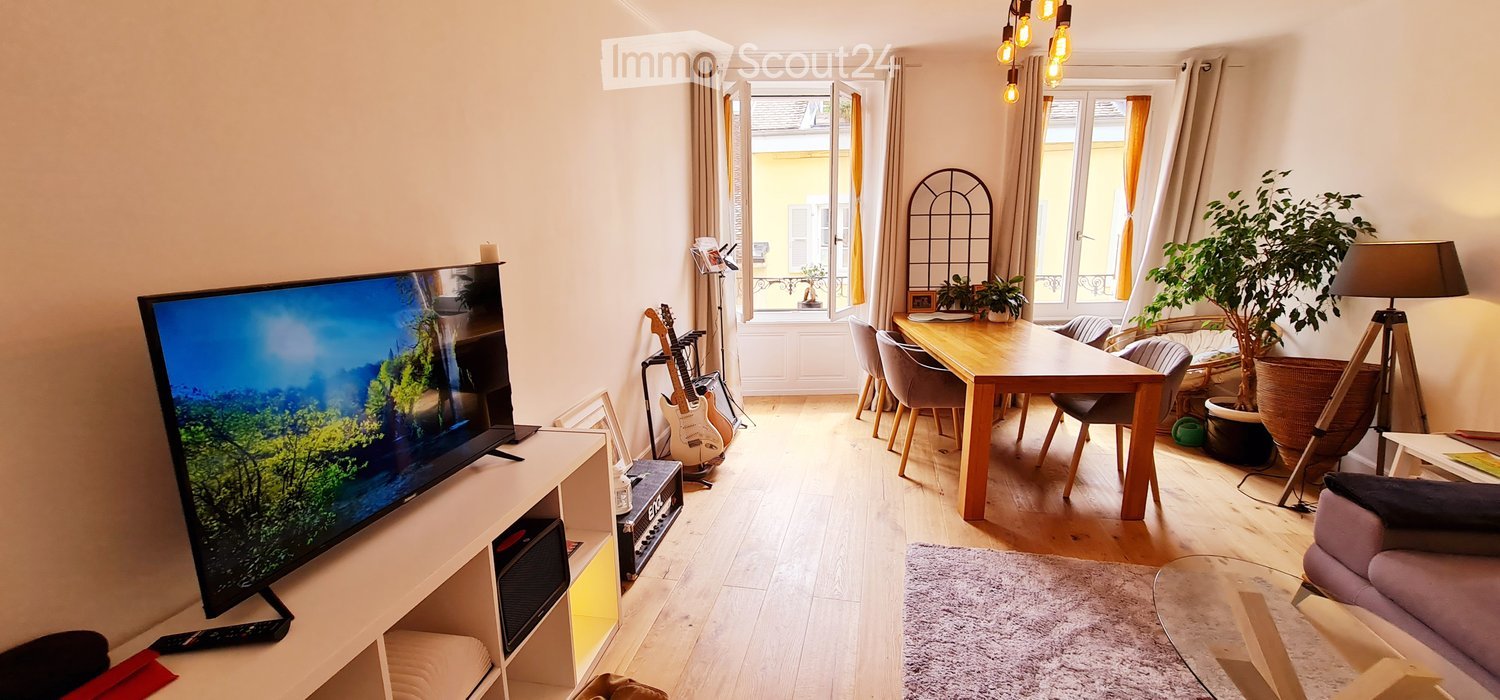 living room with wooden floor, dining table with chairs, TV, potted plants, lamps, and musical instruments