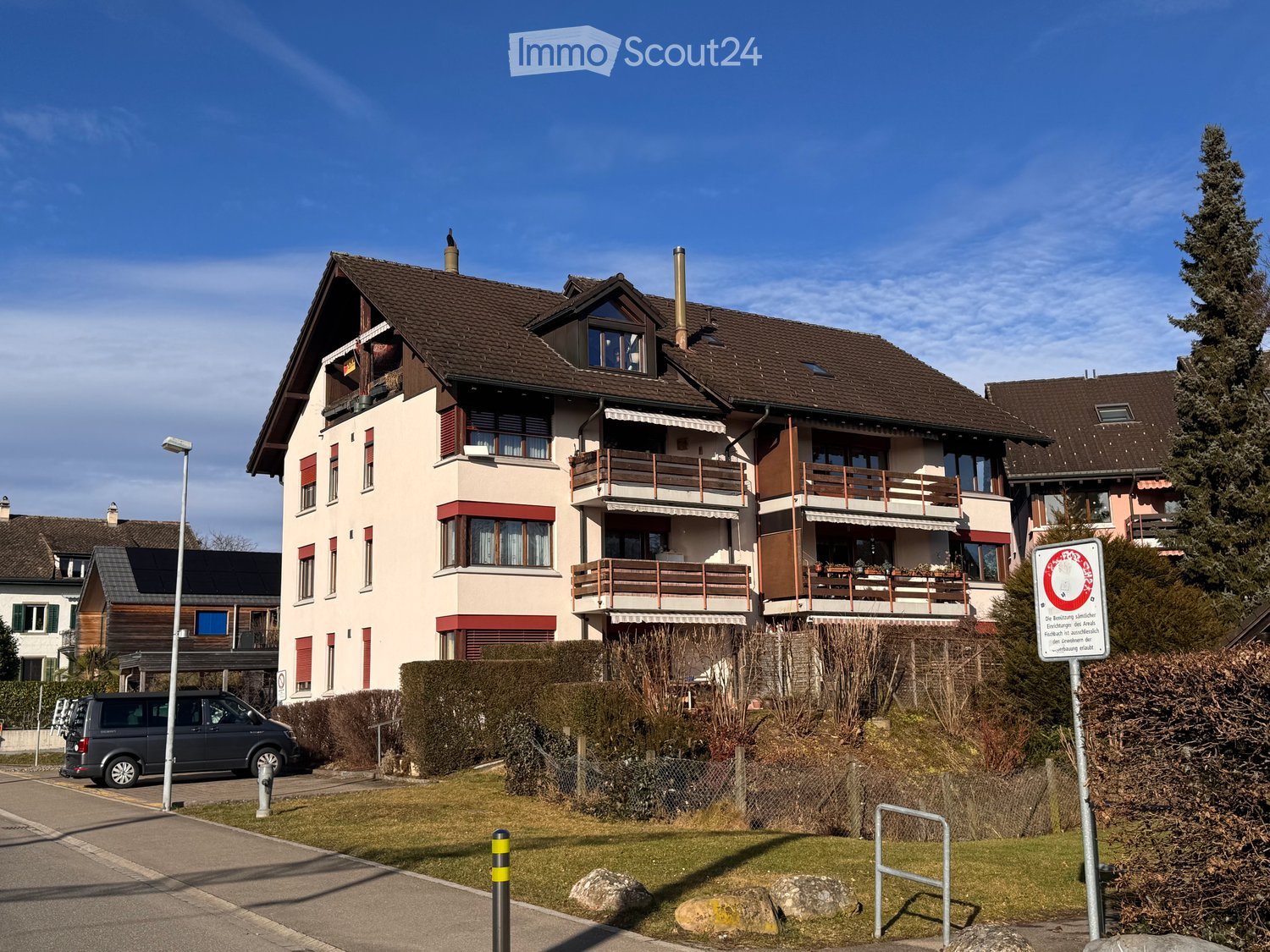 A two-story residential house with a brown tiled roof, multiple windows, balconies, and a well-maintained garden area.