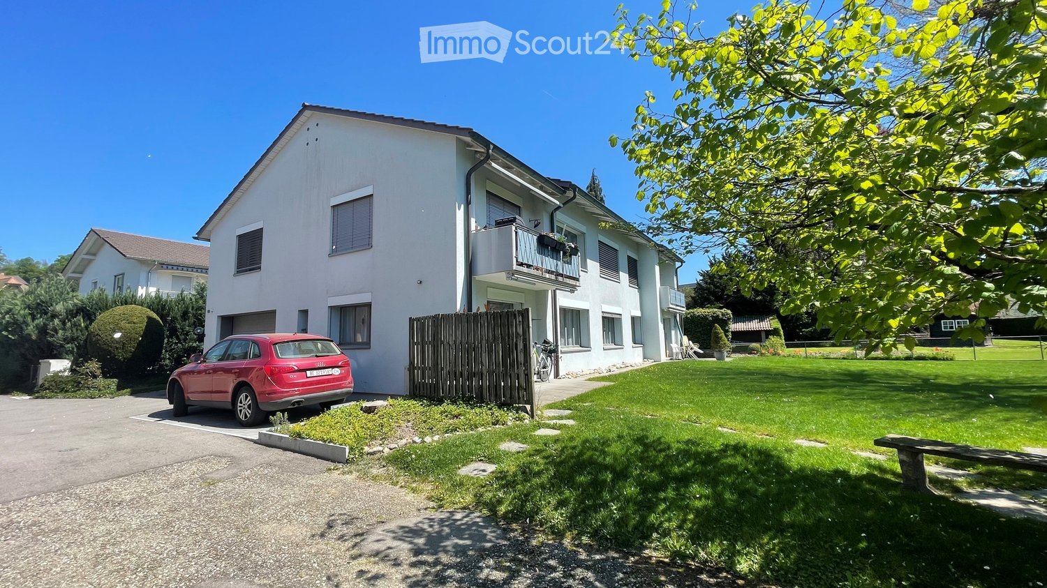 2 story house, white exterior, balcony, red car parked in front, wooden fence, green lawn, trees