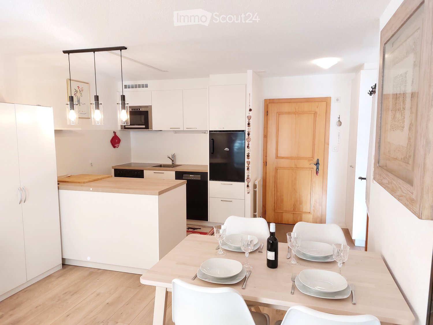 modern kitchen with dining area, white cabinets, wooden floor, dining table, wine bottle, wine glasses, plates, forks, knives, microwave, dishwasher
