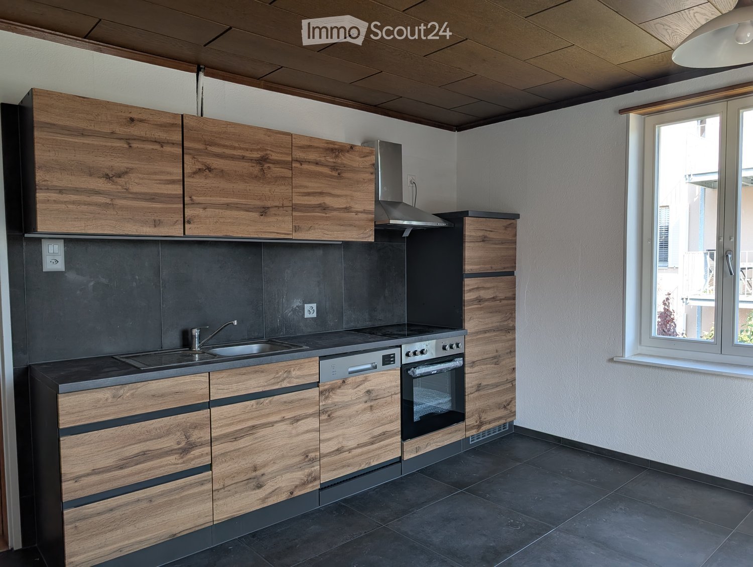 Modern kitchen with wooden cabinets, stainless steel appliances, and dark countertops.