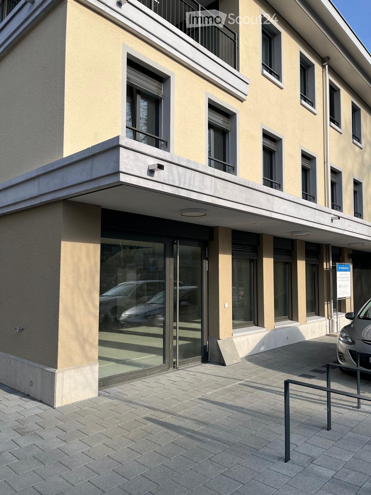 Modern building with glass facade, balcony, and parking area