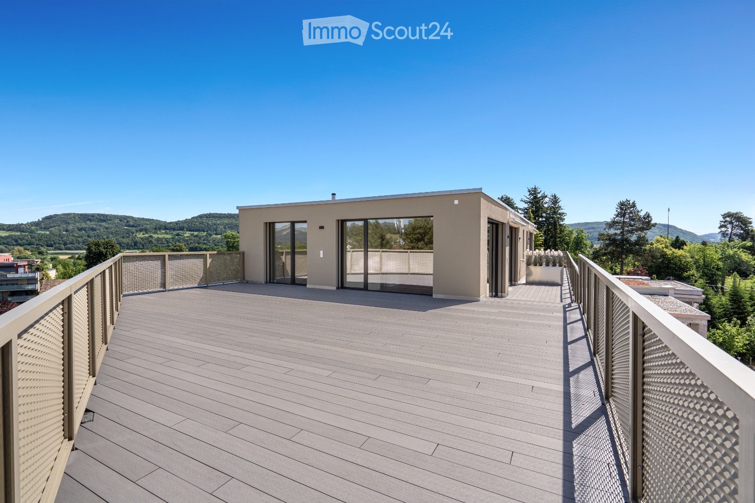 Modern rooftop terrace with wooden decking, metal railings, and panoramic views of a green landscape and hills.
