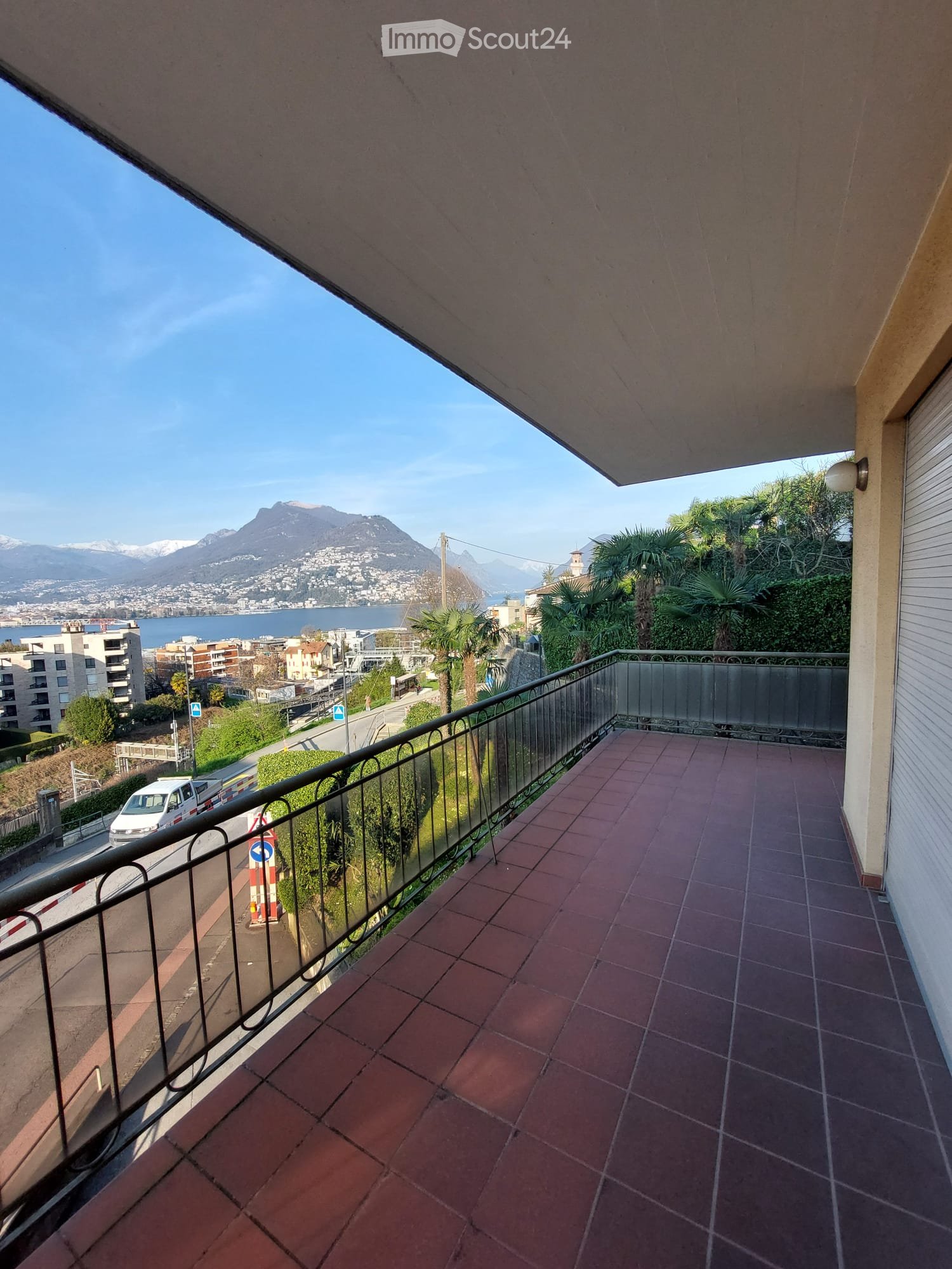Balcony with tiled floor, black railings, overlooking a road and a lake