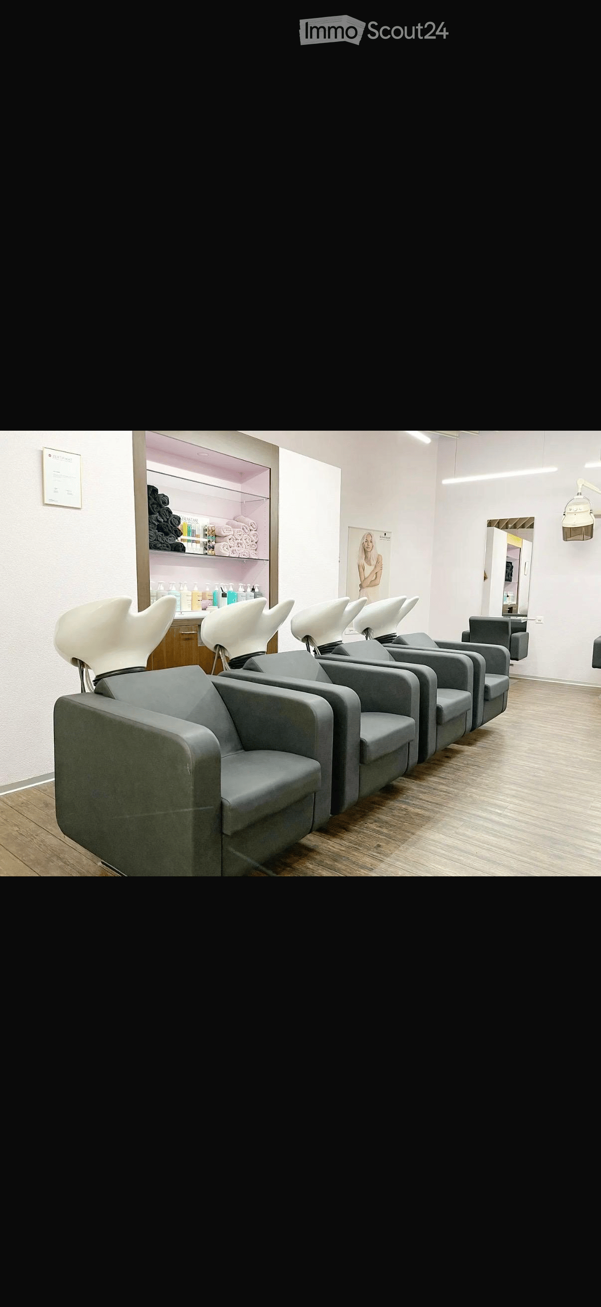 A salon with a row of grey chairs, a wooden floor, a white wall, a shelf with products, and a mirror.