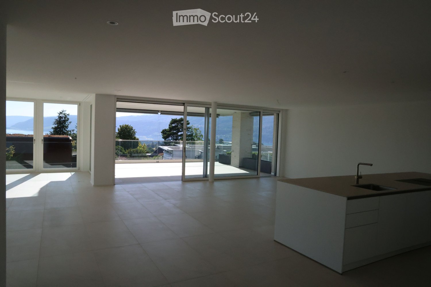 Empty kitchen with tiled floor, white cabinetry, and large sliding glass doors opening to a balcony with scenic mountain view.