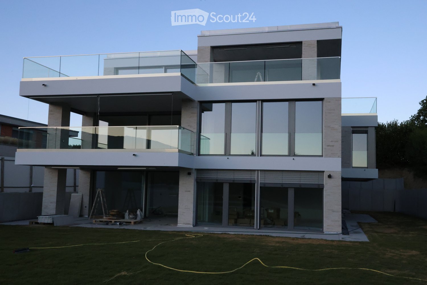 Modern two-story house with large glass windows and balconies, featuring a raised ground floor and contemporary design.