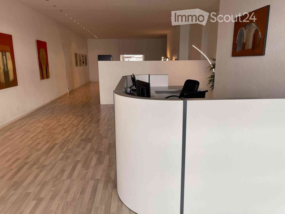 empty room, wooden floor, white walls, reception desk, computer monitors, black office chair, paintings on the wall, arched lamp