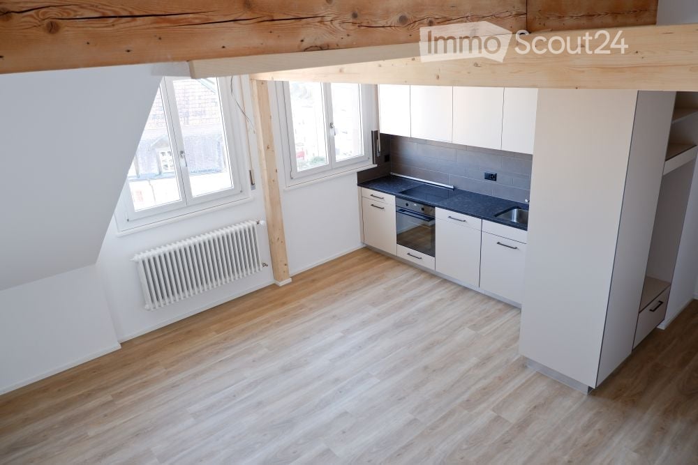 empty kitchen with wooden floor, white cabinets, black countertop, white radiator, windows