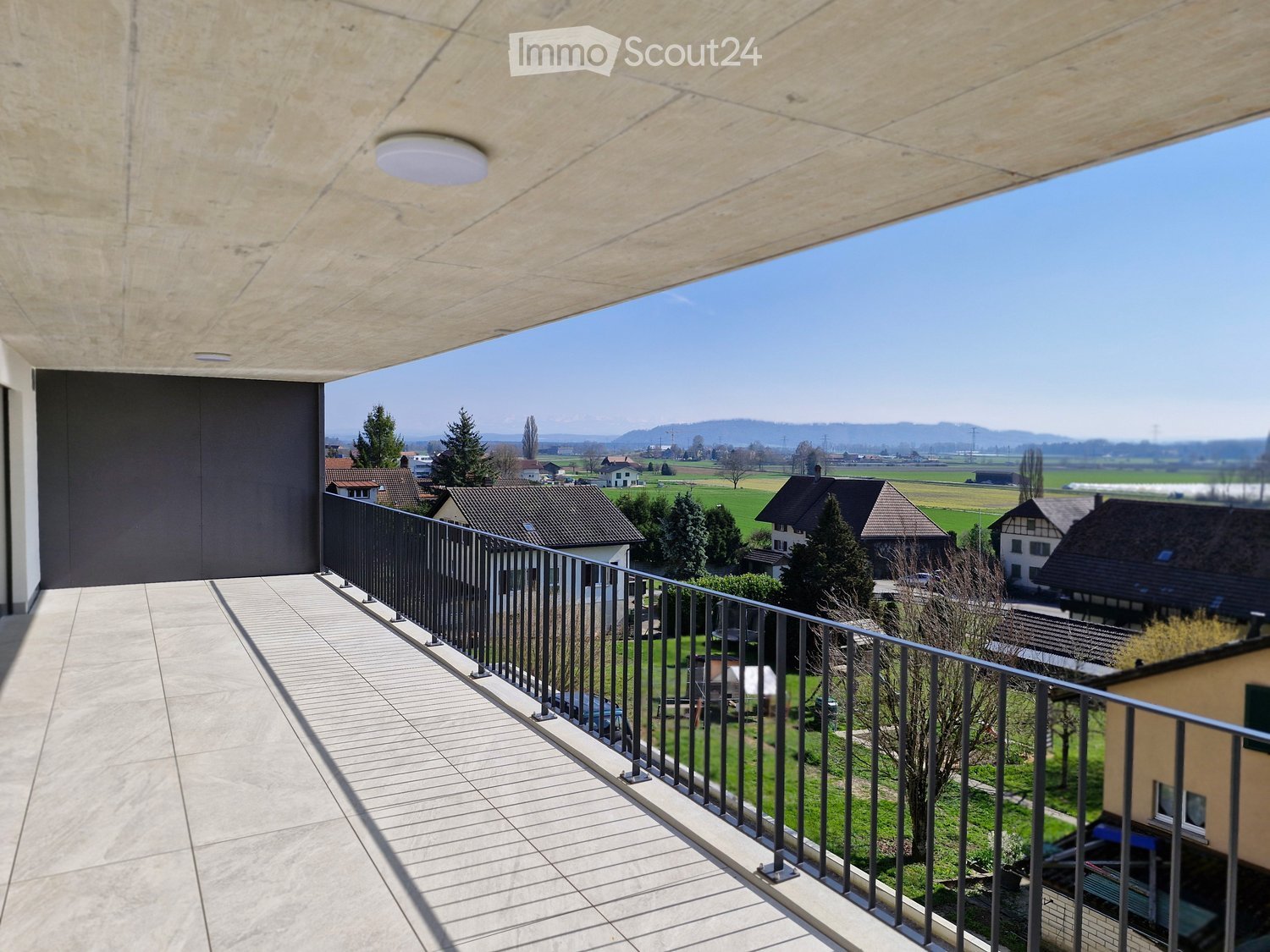 large balcony with tiled floor, black railings, view of the countryside