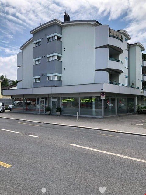 4 story building, gray exterior, glass windows, balcony, glass doors, plants, cars parked