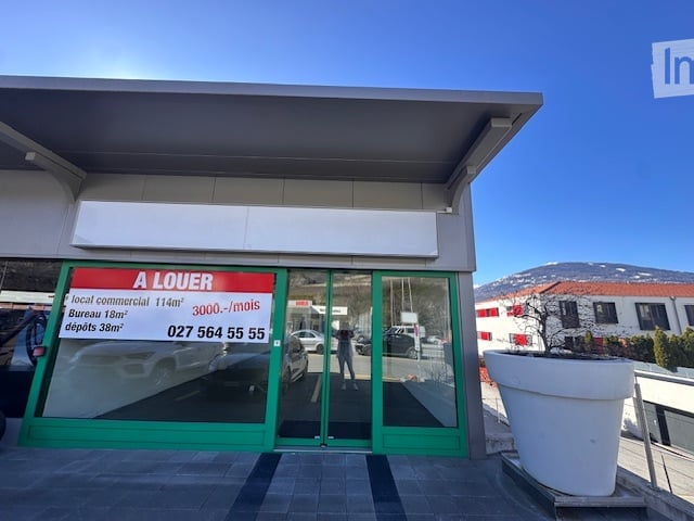 Commercial building with glass doors and windows, green frame, signboard, and a large white planter