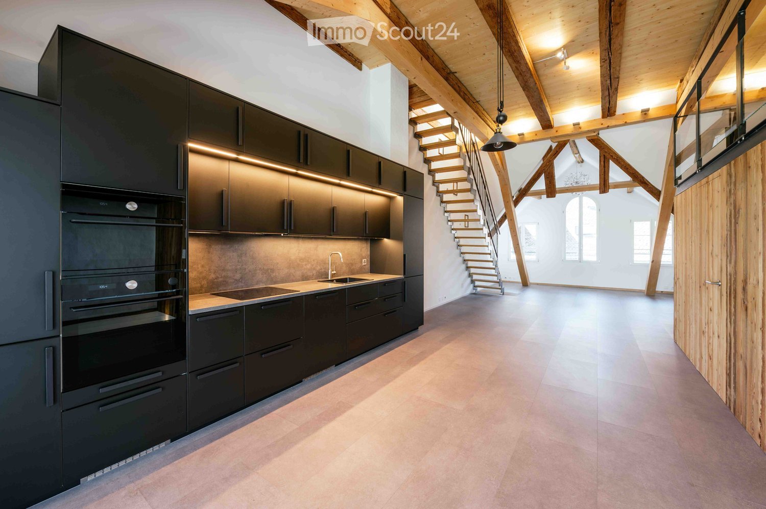 Modern kitchen with black cabinets, stainless steel appliances, and a sleek design, featuring a staircase leading to an open loft area.
