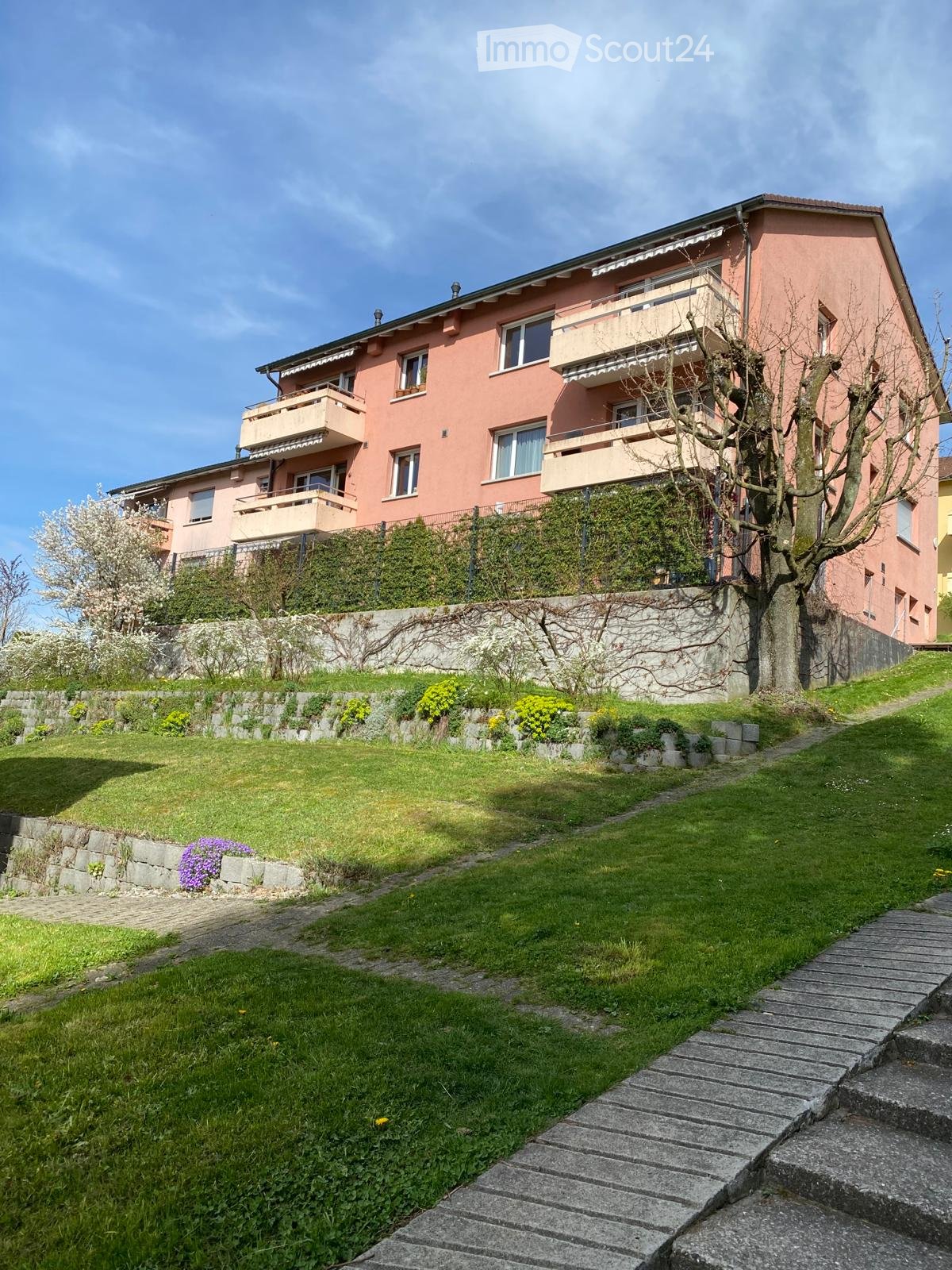 3 story house, pink exterior, multiple balconies, stone wall, green lawn, tree