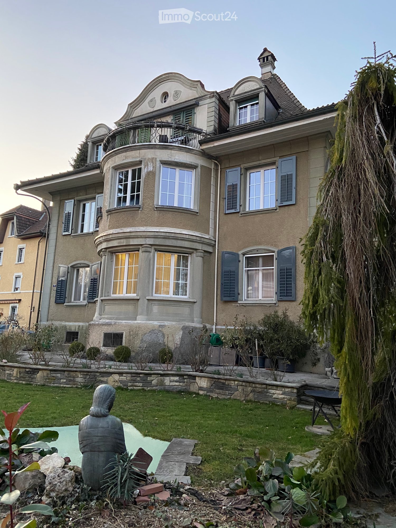 Large house with multiple windows, balcony, garden, and a small pool