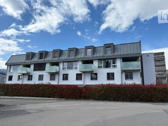 A modern apartment building with multiple balconies, white exterior, and a gray roof