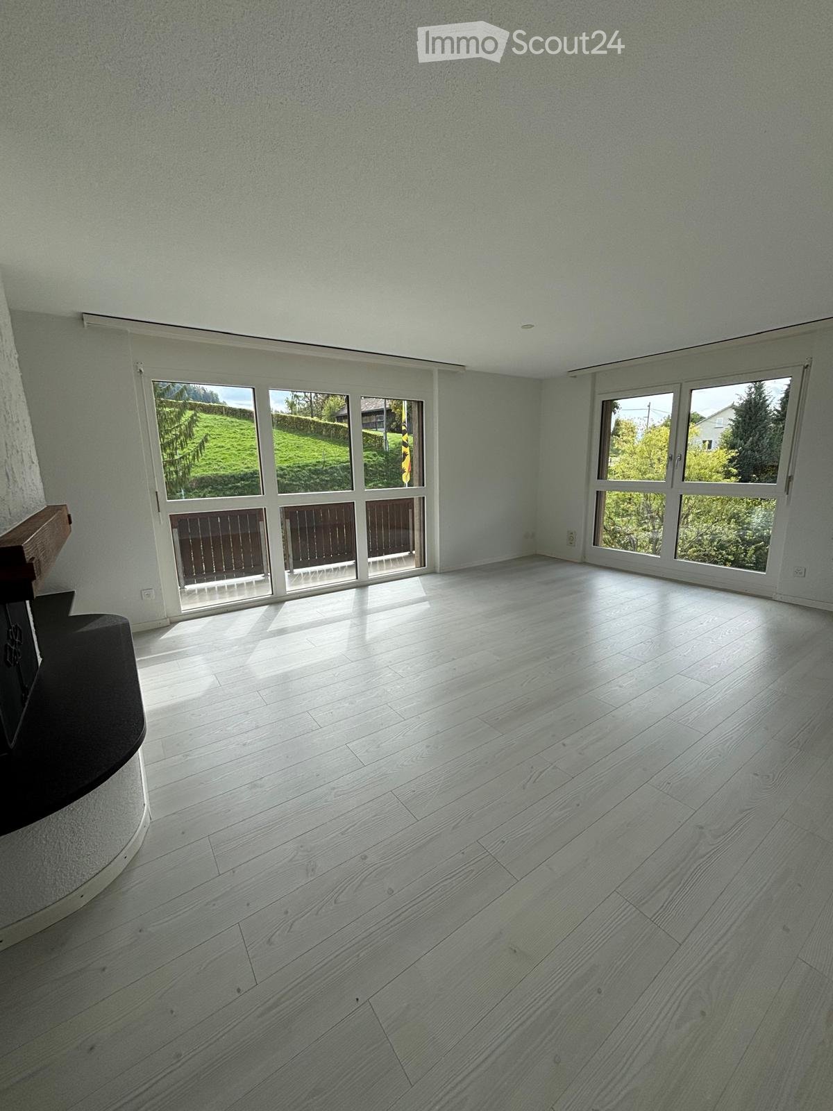 Empty room with light-colored wooden flooring, large windows, and a view of a green landscape.