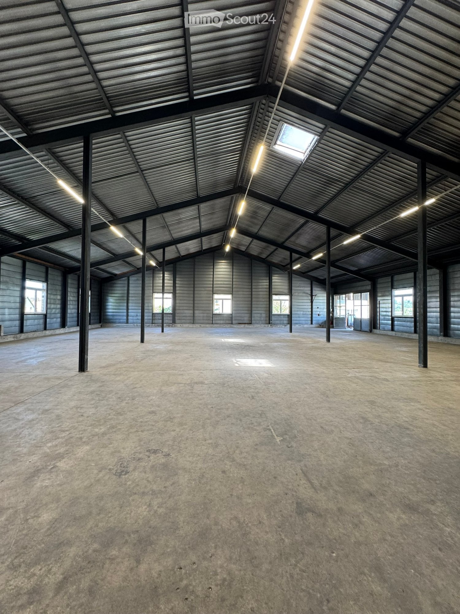 Empty industrial-style room with concrete floor, metal ceiling, and large windows, no furniture or equipment.