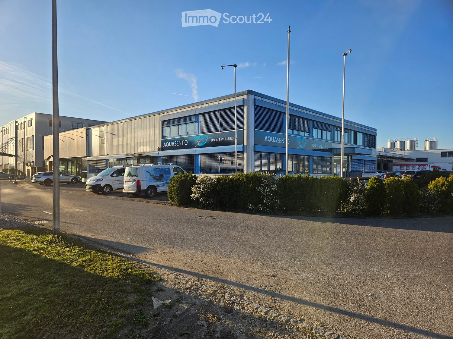 Commercial building with a sign reading Aquasento Pool & Wellness, multiple cars parked in front, modern architecture, large windows, and a flat roof.