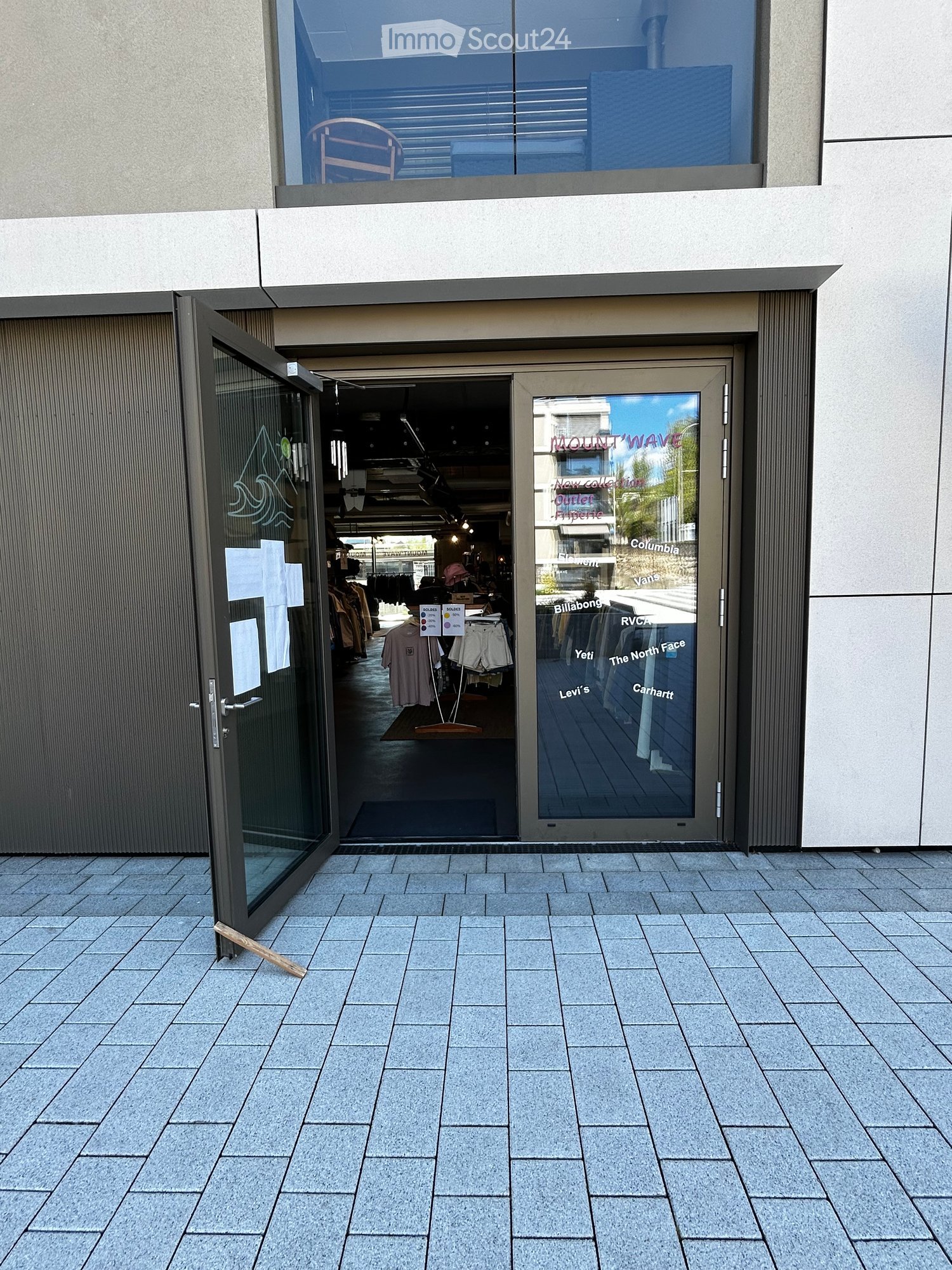 Open entrance to a building with a glass door, a small rug, and a display of clothing inside.