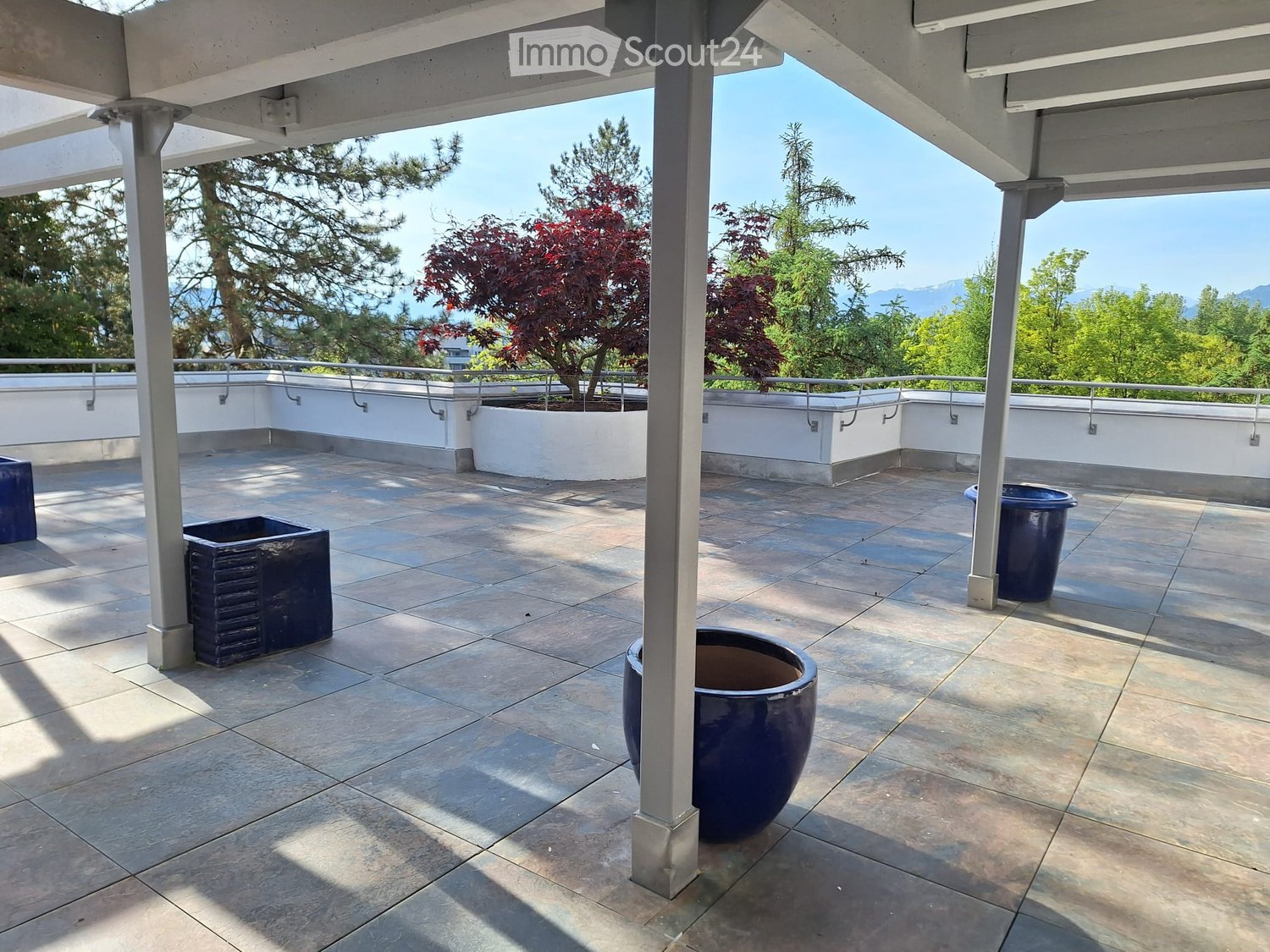 A covered terrace with a tiled floor, metal railings, and four blue planters.