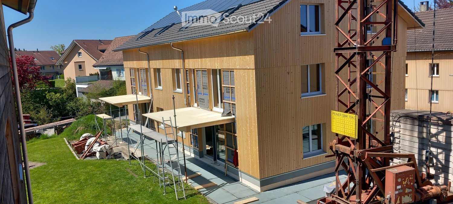 Newly constructed house, wooden exterior, solar panels on the roof, scaffolding around the building, construction crane nearby