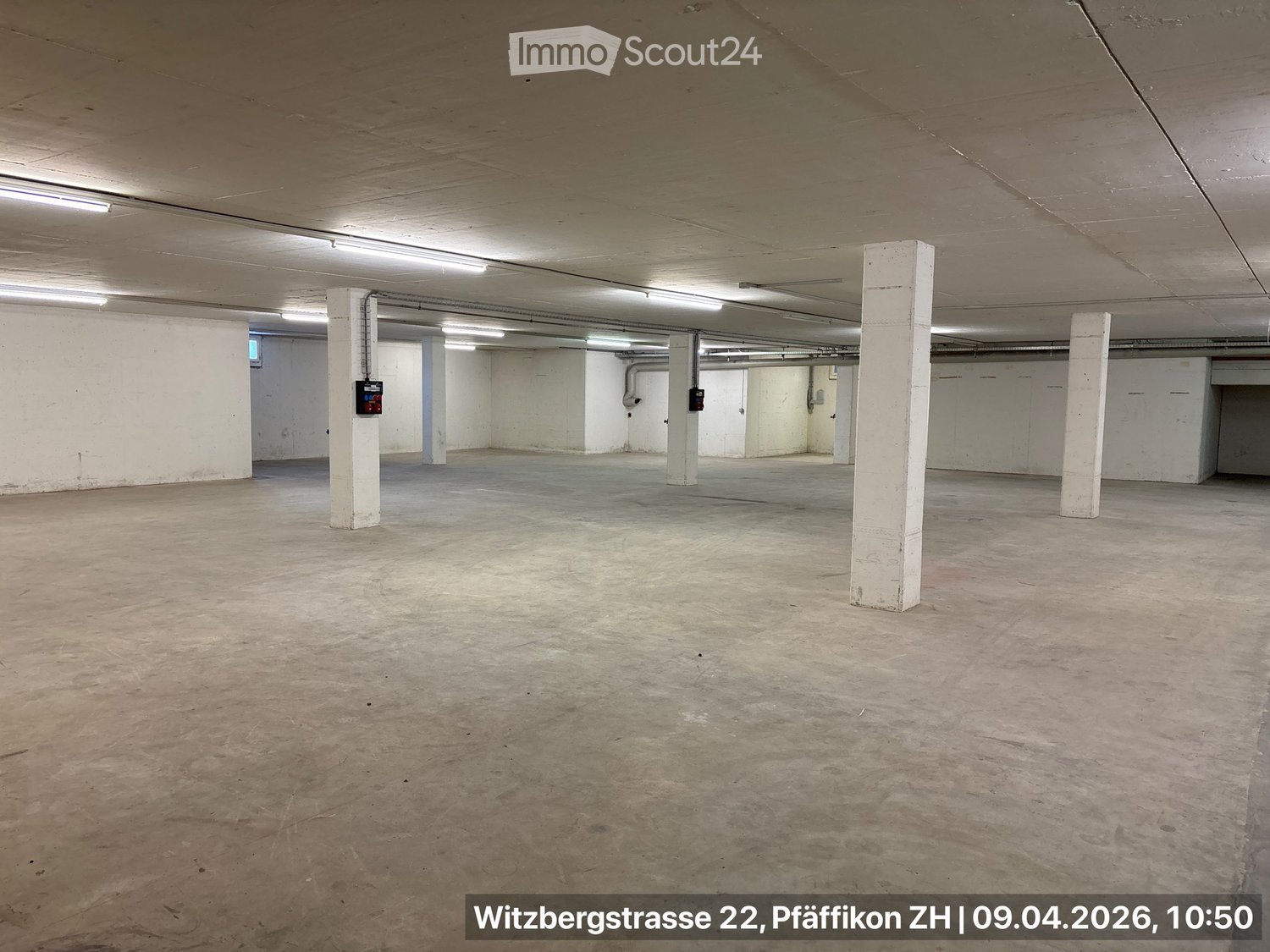 Empty parking lot with white walls, concrete floor, and white pillars, with lights on the ceiling.