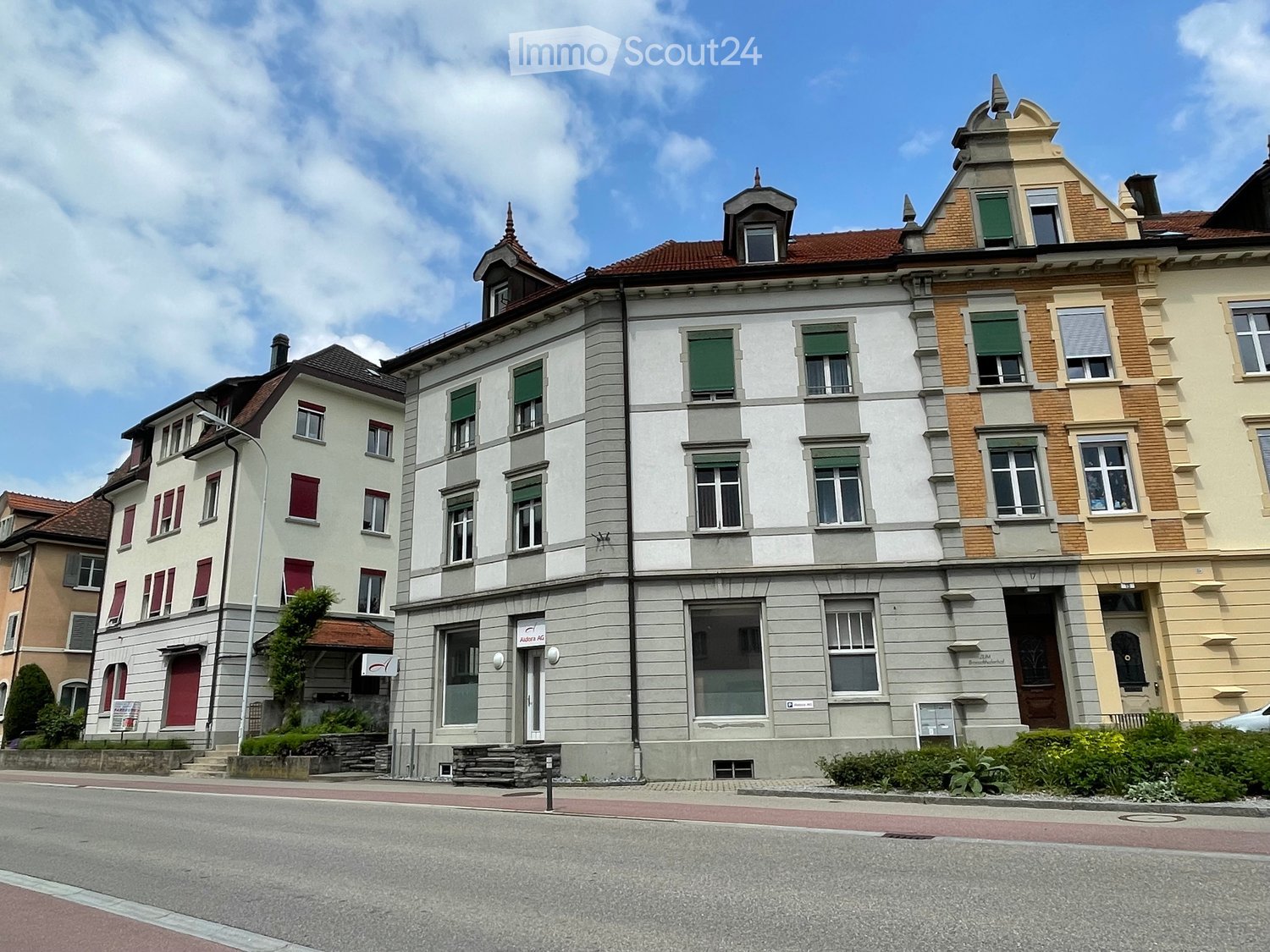 A row of multi-story buildings with red roofs and white walls, each with multiple windows and red shutters, a streetlight, and a car parked in front.