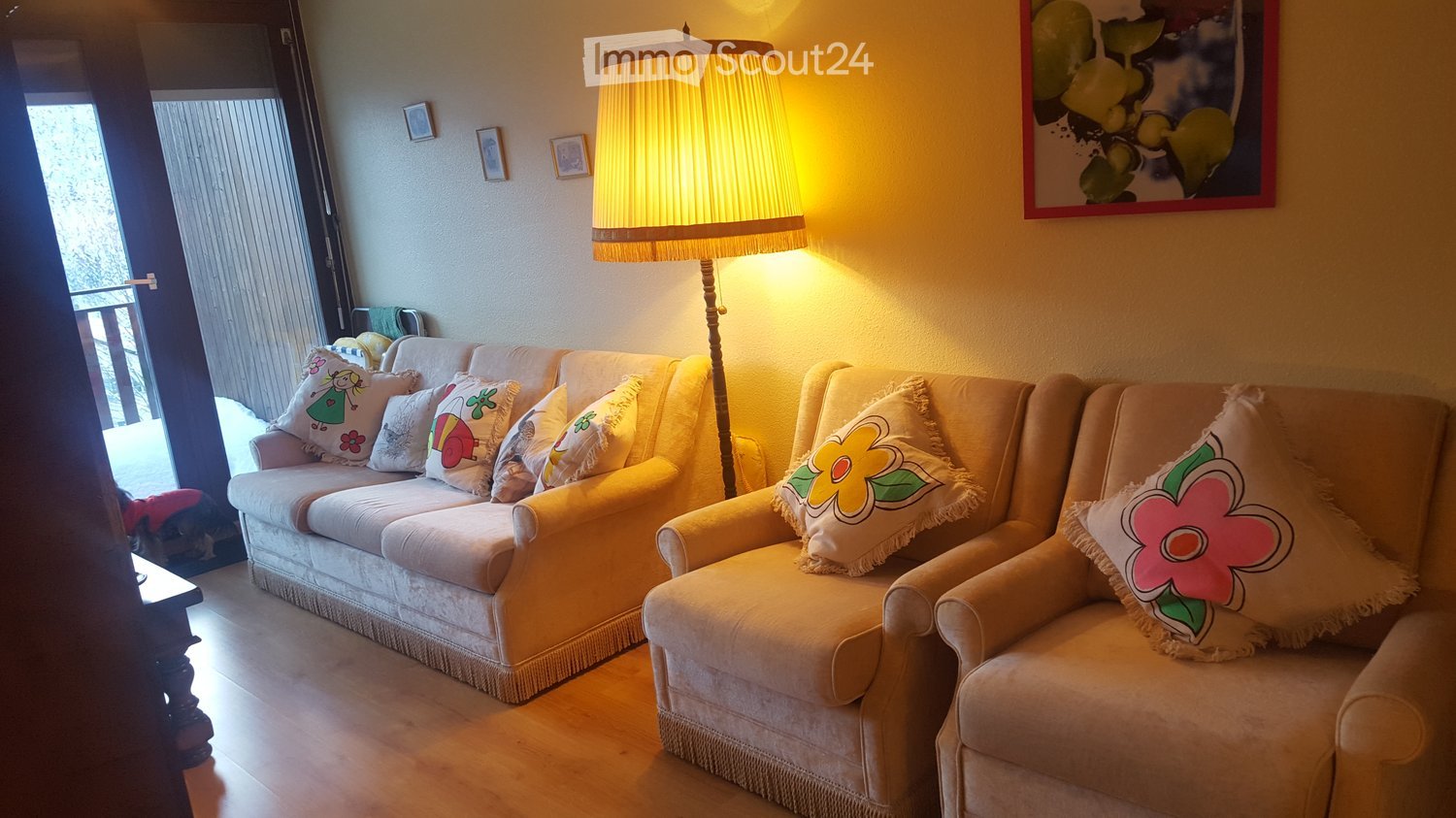 living room with sofa, armchairs, lamp, pillows, picture frames, wooden floor, door