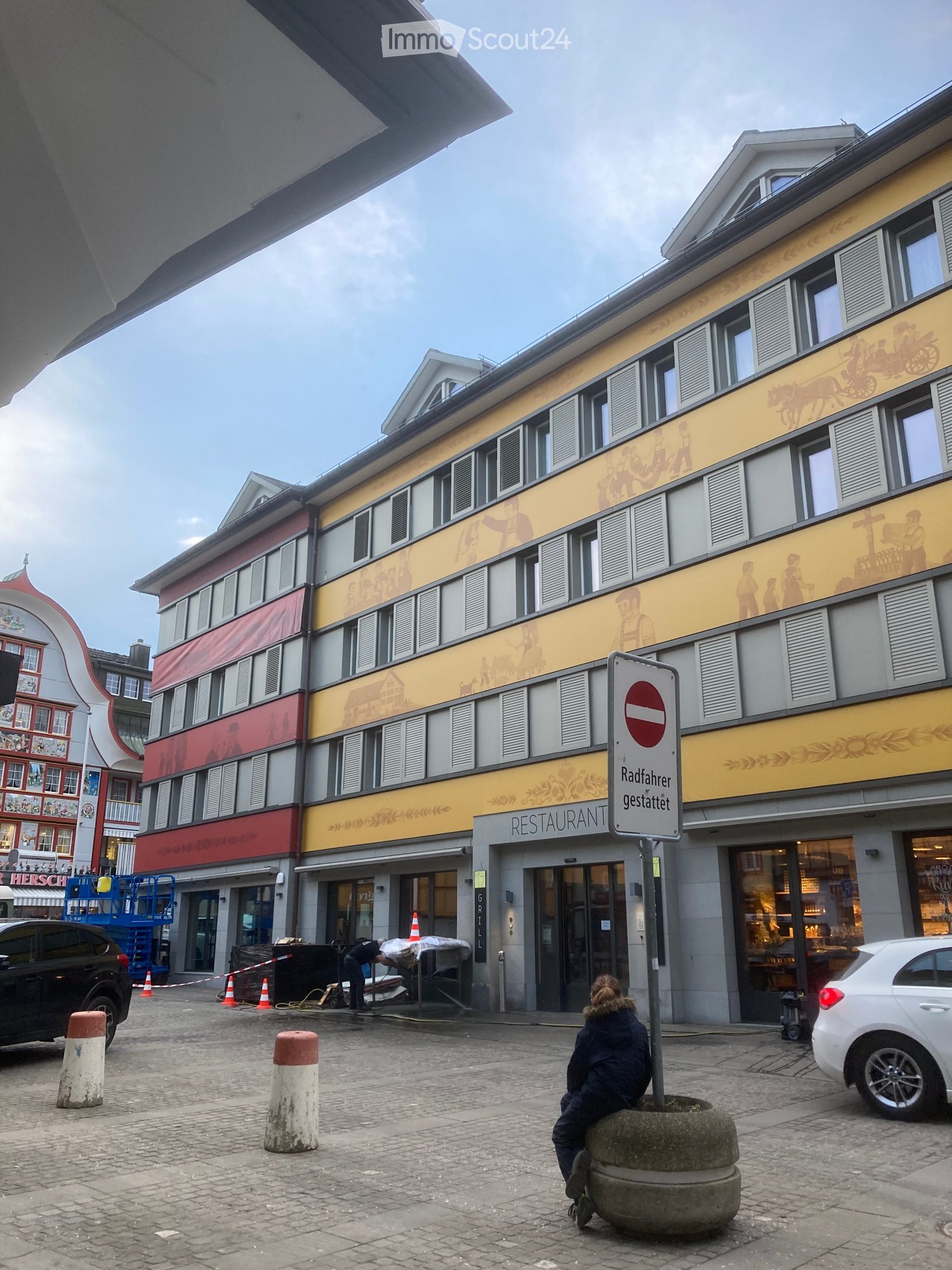 A multi-story building with a restaurant on the ground floor, featuring a yellow and red facade with illustrations, multiple windows, and a sign indicating a restaurant.
