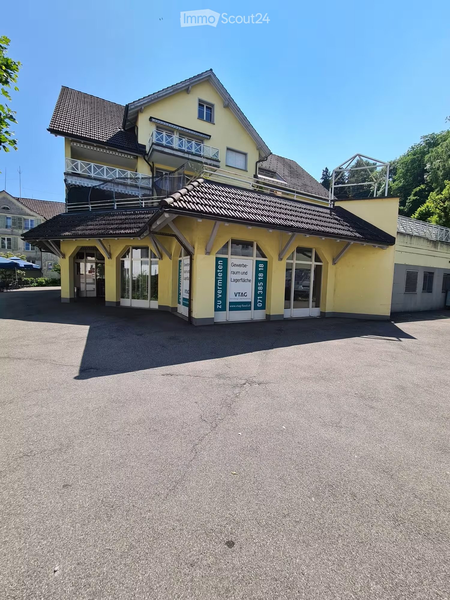 2 story yellow house, brown roof, large windows, balcony, parking lot in front
