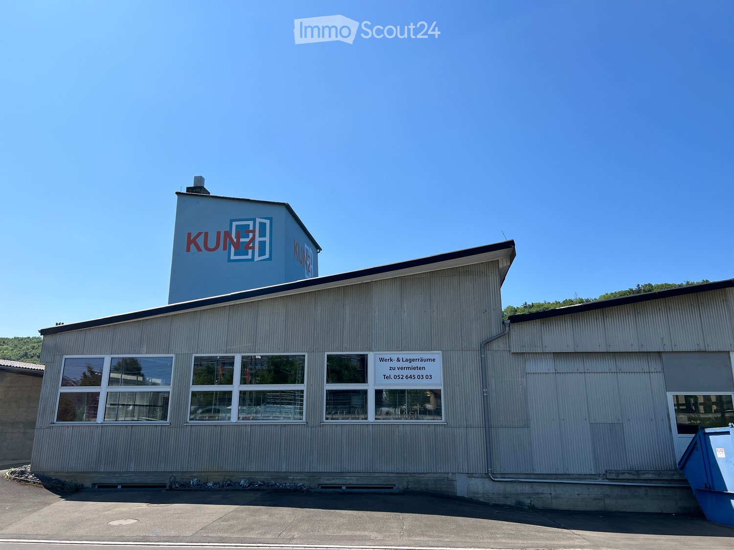 Industrial building with a sign reading 'KUNZ', multiple windows, and a smaller building on top