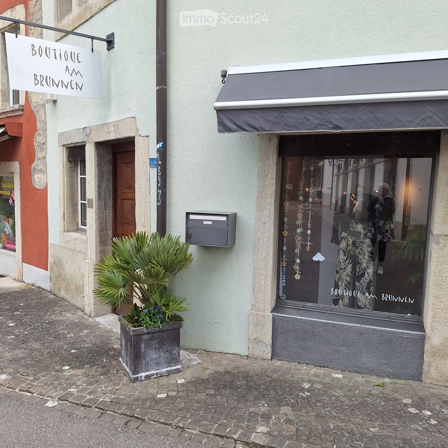 Facade of a building with a sign, a mailbox, a potted plant, and a shop window.