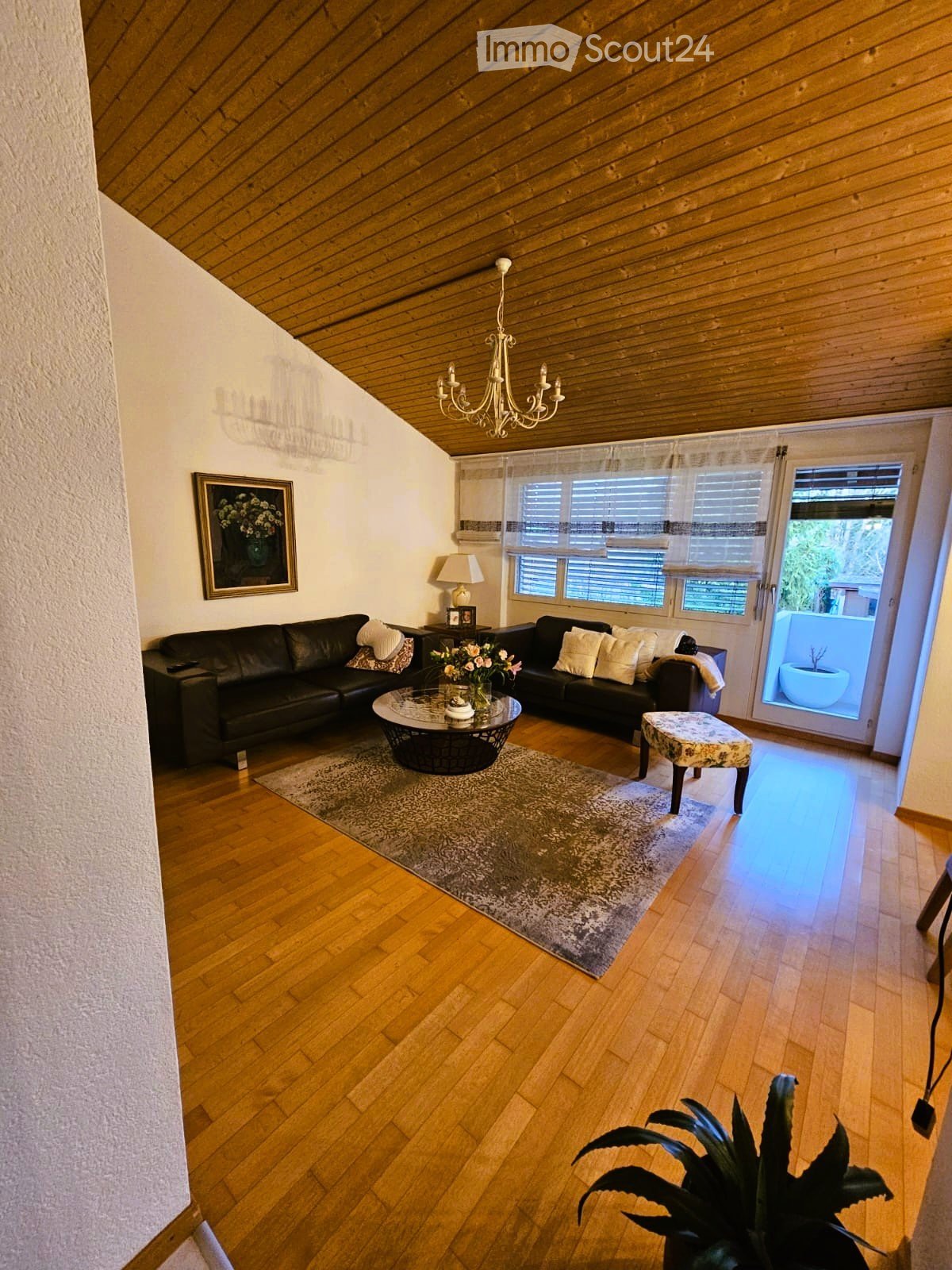 living room with wooden floor, chandelier, black leather couches, coffee table, rug, picture frame, lamp, ottoman, potted plant, balcony