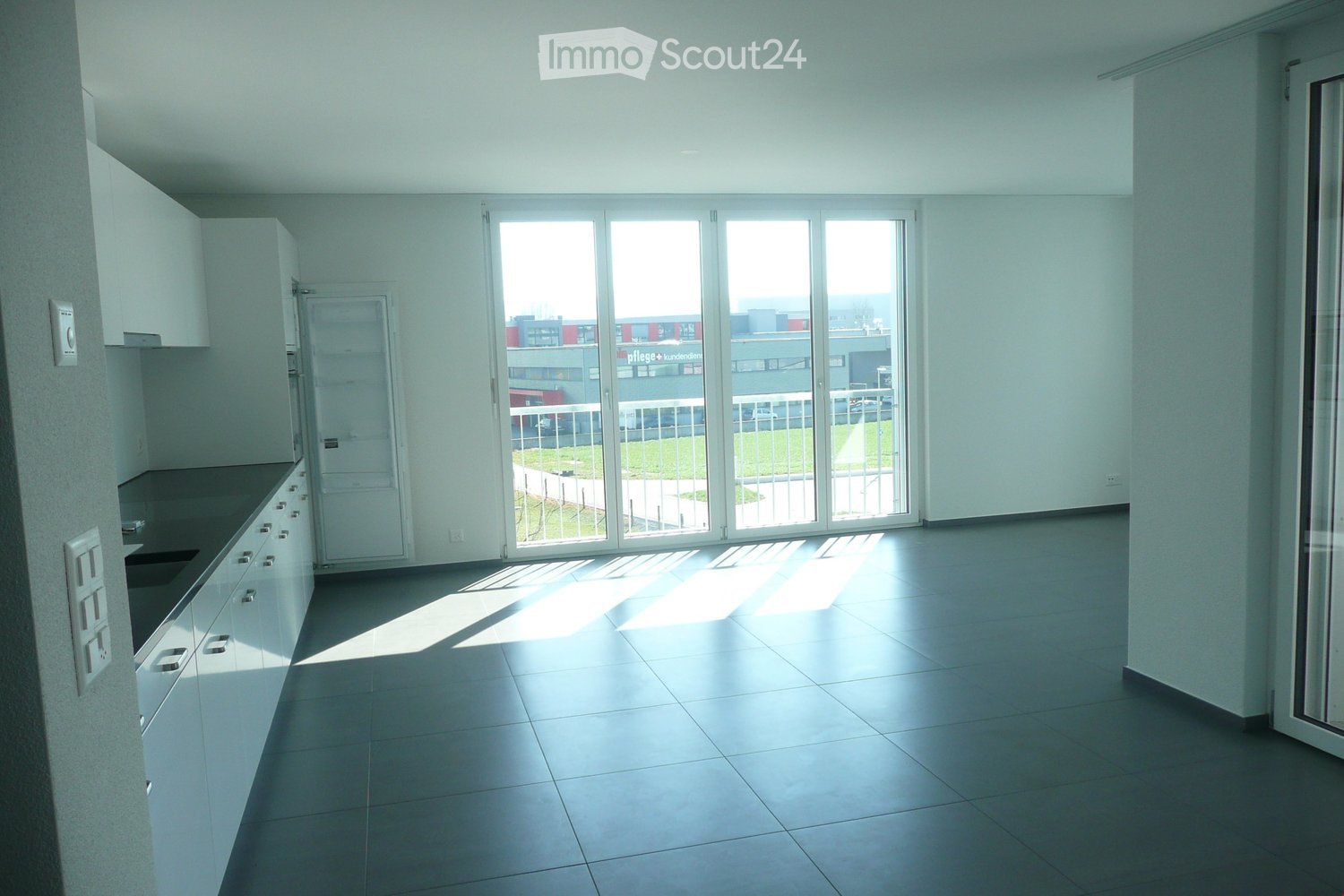 Empty kitchen with white cabinets, black countertops, and a large sliding glass door leading to a balcony.