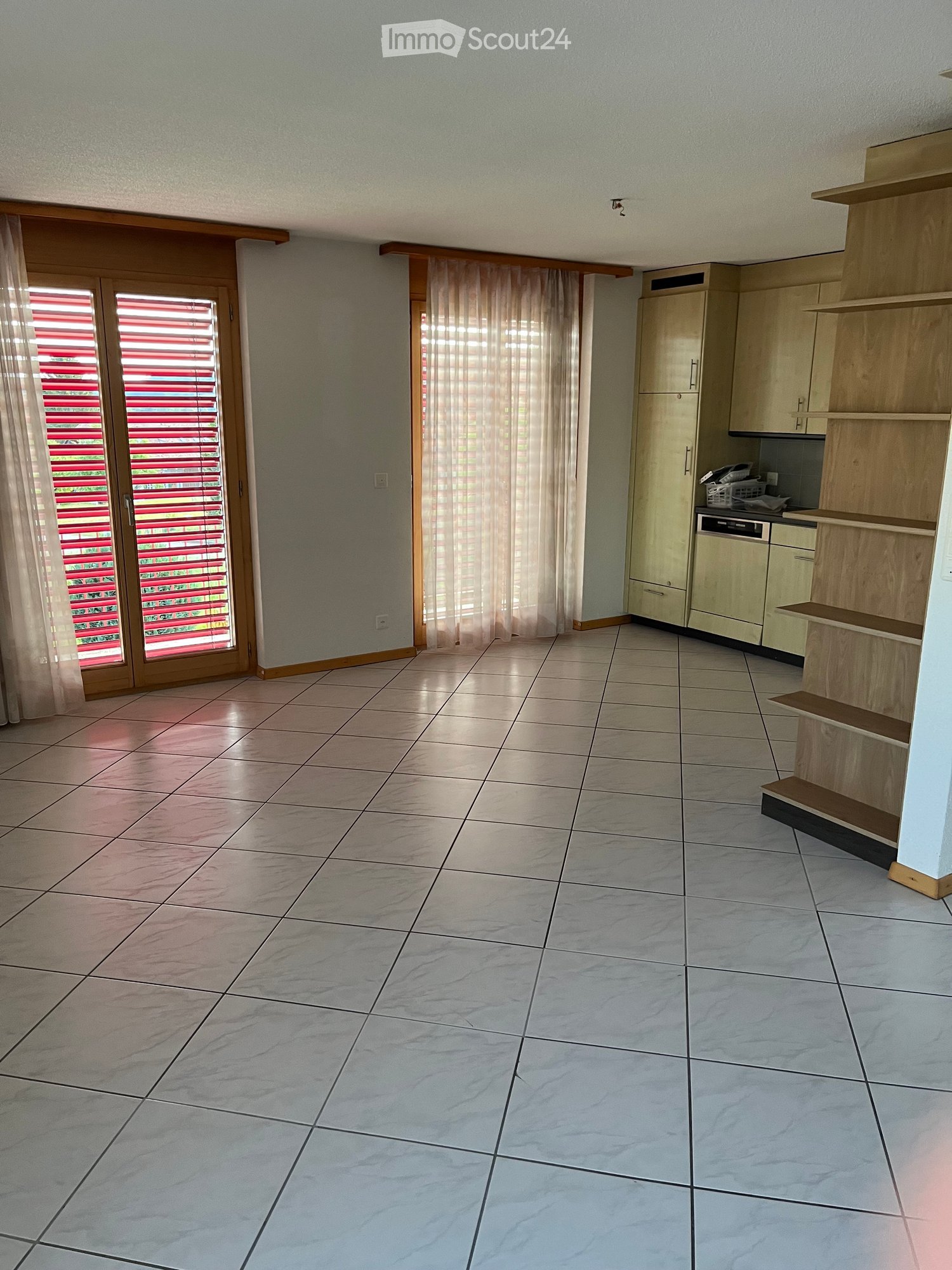 Empty kitchen with tiled floor, light-colored cabinets, and a window with blinds. No furniture or appliances are present.